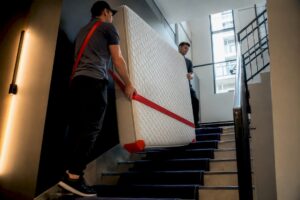 Movers carrying mattress upright through stairwell
