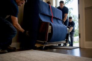 Crew guiding a padded piano through doorway